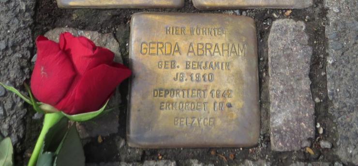 Metallplatte mit Inschrift im Straßenbelag eingelassen, daneben eine rote Rose