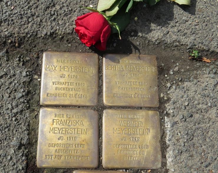 vier Metallplatten mit Inschrift im Straßenbelag eingelassen, daneben eine rote Rose