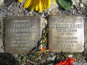 zwei Metallplatten mit Inschrift im Boden eingelassen, daneben eine rote und eine gelbe Blumese