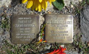 zwei Metallplatten mit Inschrift für Helene Langer und Therese Zuckerkandl im Boden inmitten von Pflastersteinen eingelassen, daneben eine rote und eine gelbe Blumese
