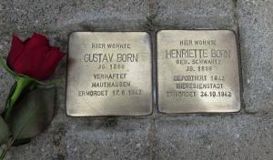 zwei Metallplatten mit Inschrift im Boden inmitten von Pflastersteinen eingelassen, daneben eine rote Rose