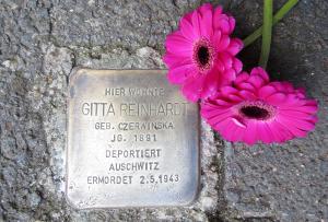 Metallplatte mit Inschrift im Straßenbelag eingelassen, daneben zei rote Gerbera